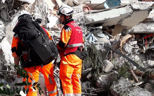 Two men oft he Swiss Humanitarian Aid Unit in front of a collapsed building.