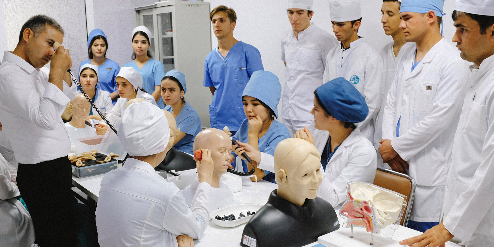 Du personnel médical tadjik effectue une formation. Sur la table se trouvent des mannequins et instruments médicaux. 
