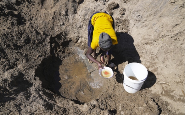 Una lugareña recoge agua de un agujero en el suelo.