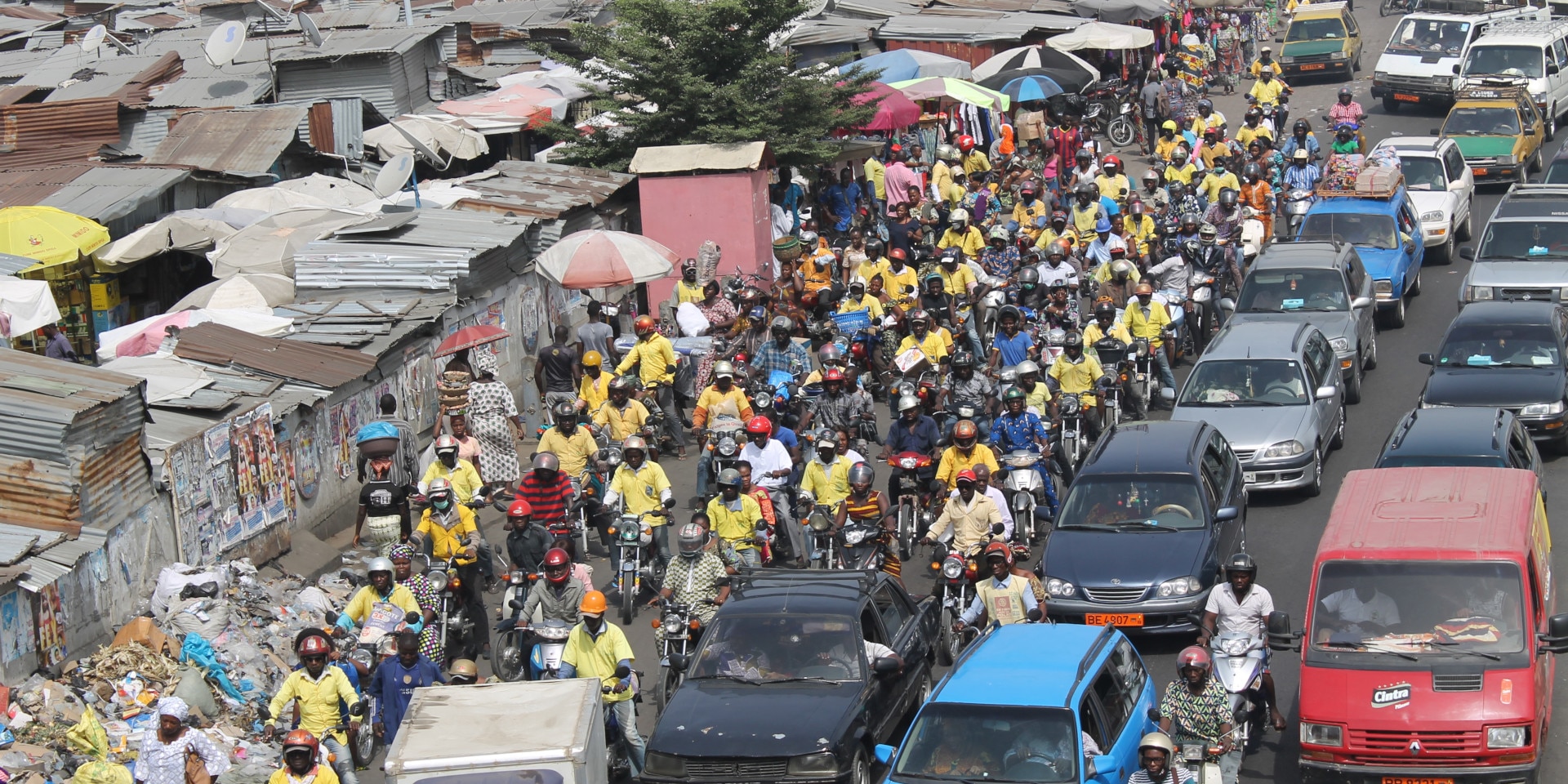 Cars and motorcycles are driving on a road in Benin. Informal housing settlements have been built next to the road.
