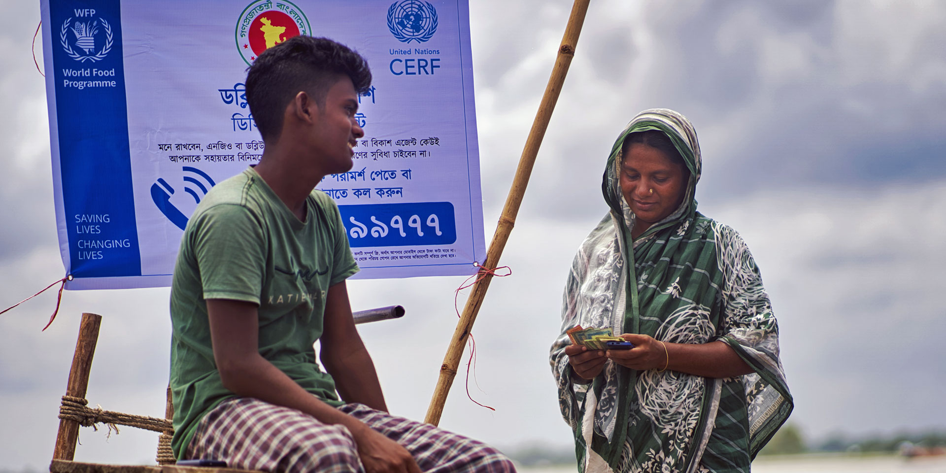 At the bank of a river in Bangladesh, a woman, with her son at her side, counts the cash assistance she received through an anticipatory action programme.