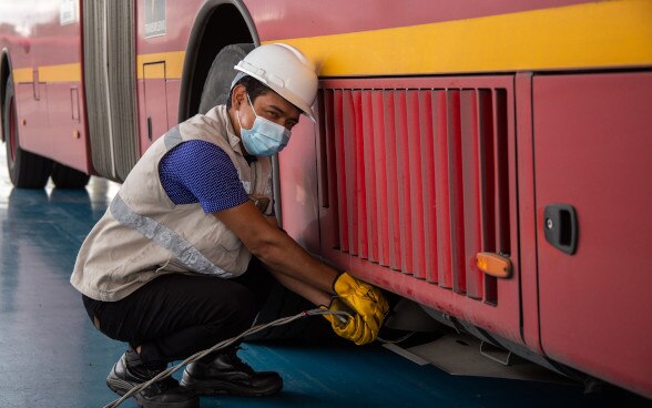 Trabajador arrodillado junto a un autobús eléctrico.
