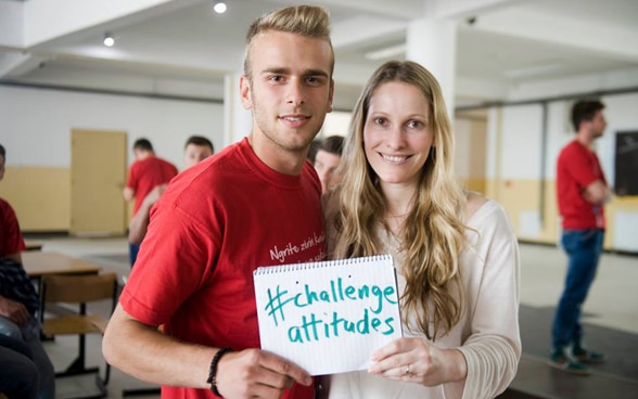 Un jeune homme et une jeune femme portant une affiche « challenge attitudes ».