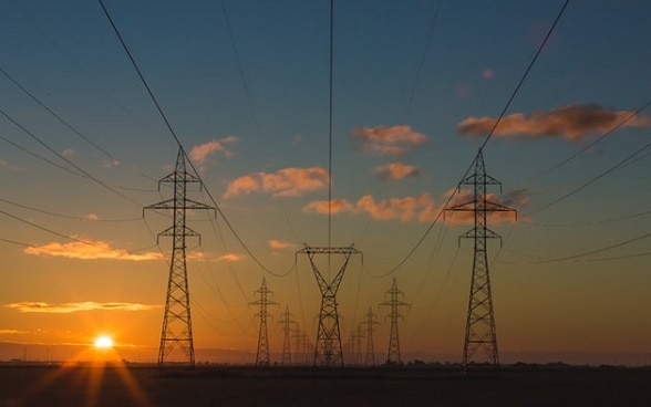 Alternativtext Plusieurs rangées de lignes à haute tension éclairées par le soleil couchant